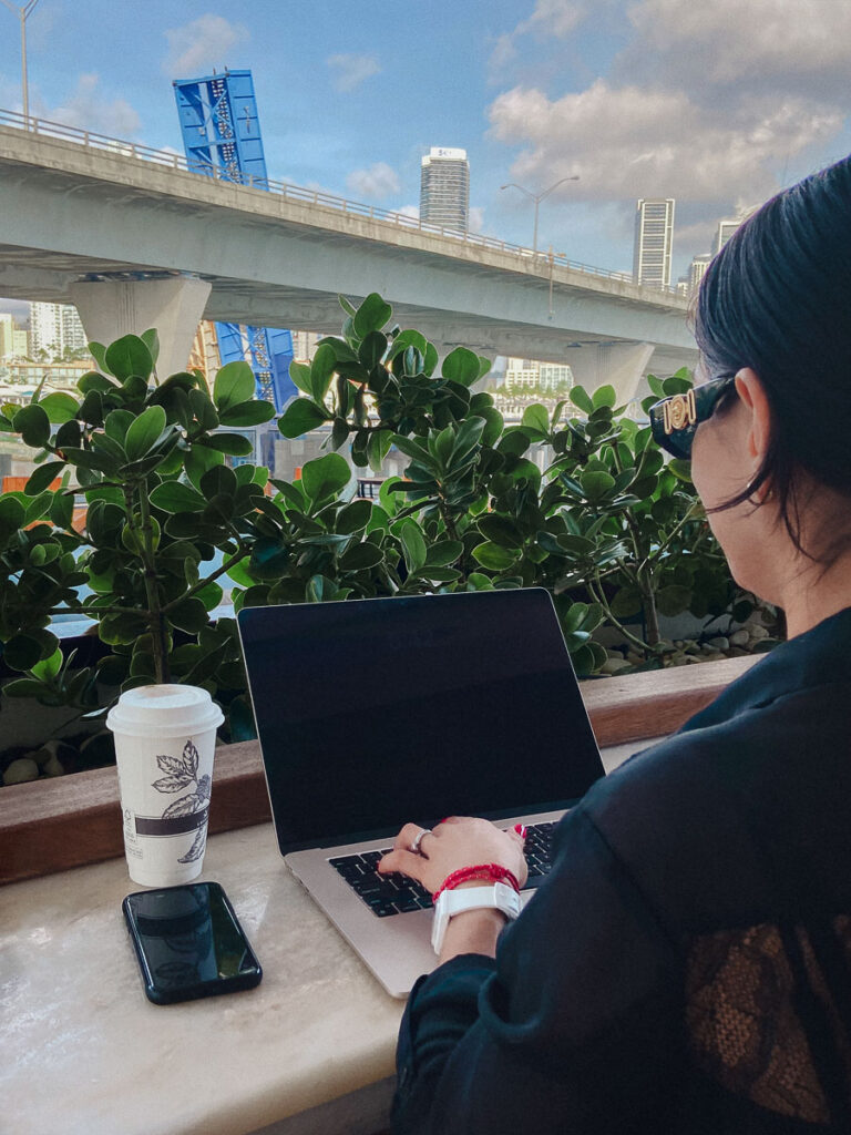 a female typing on a laptop and working from outside which is one benefit of a blog for business