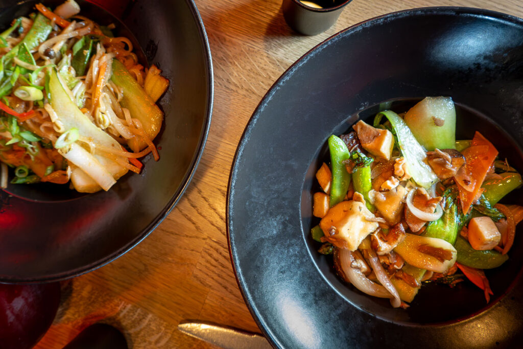 a dish of buddha delight and a stir fried rice noodles from the Virgin Voyages Lucky Lotus by Razzle Dazzle restaurant