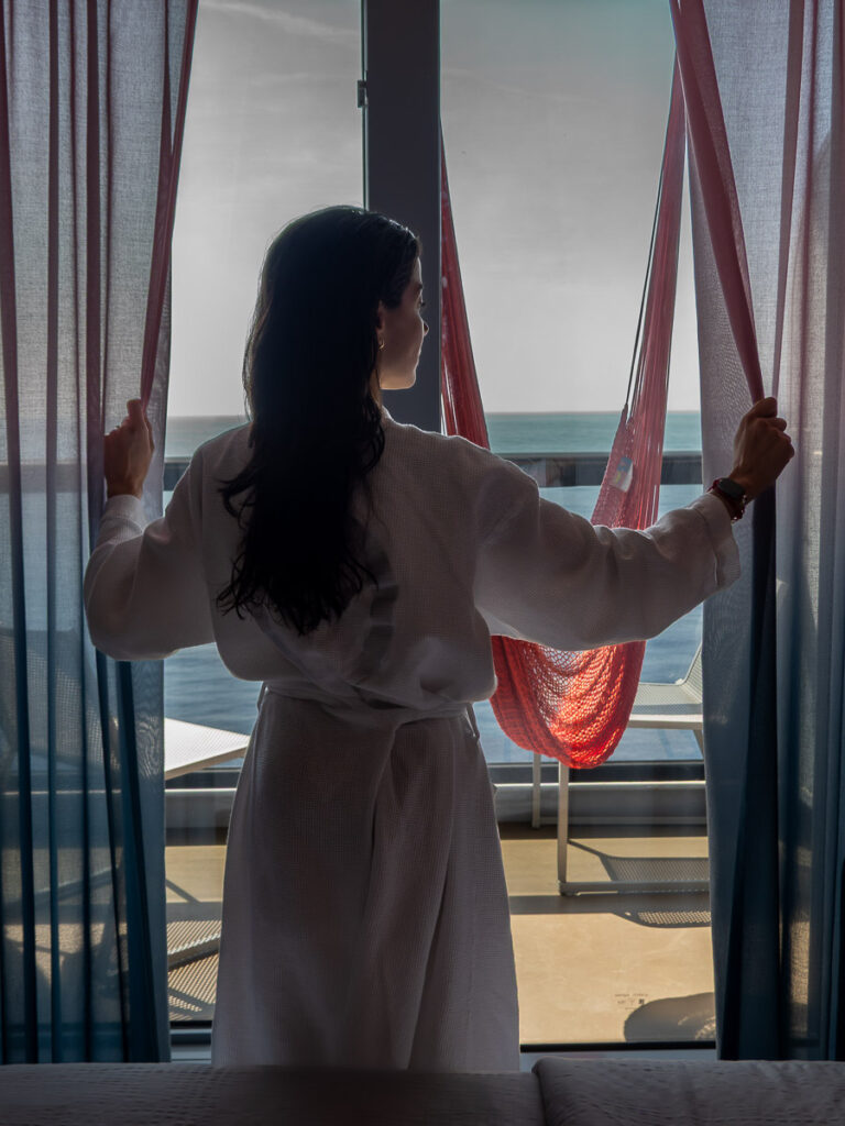 woman opening curtains with a white robe in the Virgin Voyages sea terrace cabin