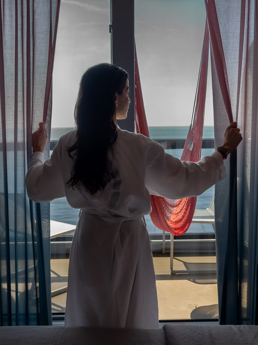 woman opening curtains with a white robe in the Virgin Voyages sea terrace cabin