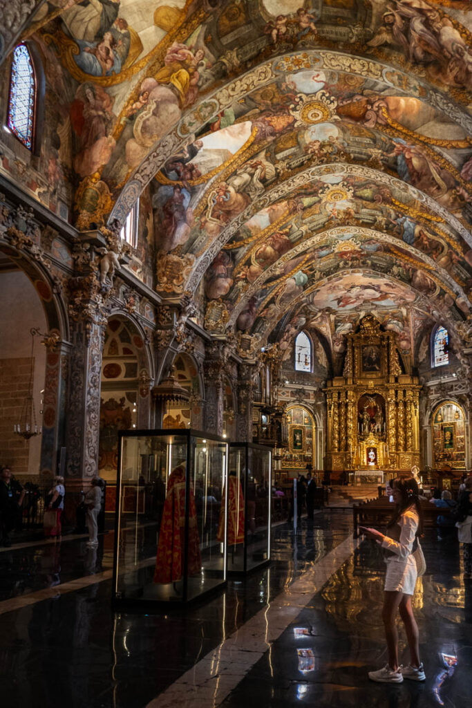 this is an image of the interior of the St Nicolas church in Valencia with its impressive fresco painted at the ceiling of the church with a gold altar and people walking