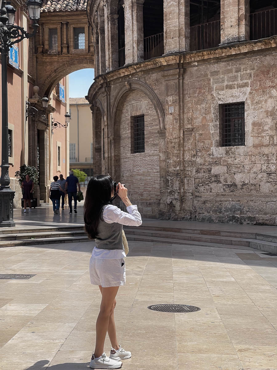 a woman taking a picture of a stone building while visiting one day in Valencia Spain