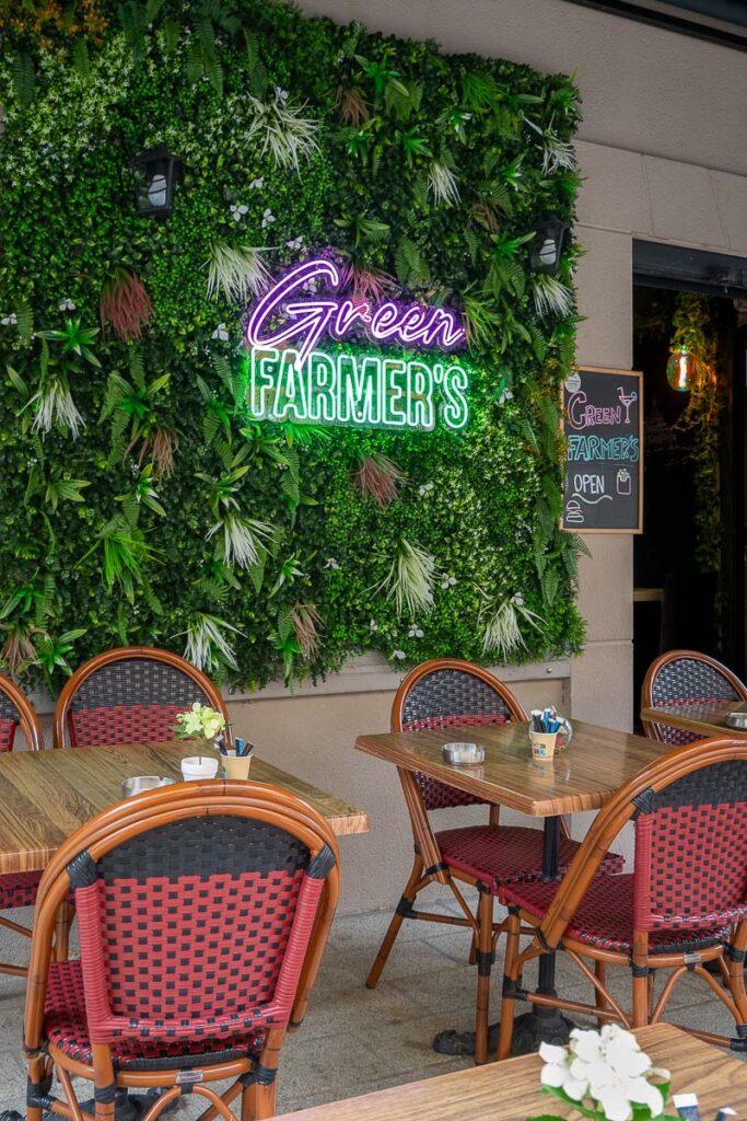 a wall with plants and dining tables which is the outdoor seating area of Green Farmer's Ajaccio Corsica cruise port a restaurant vegan