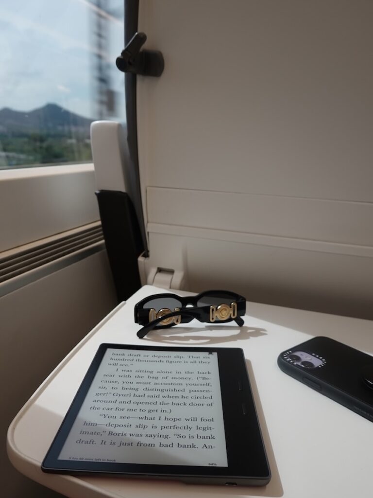 a kindle, glasses and a mobile on the seat table of the Euromed train which is How to get from Barcelona Airport to Valencia by train