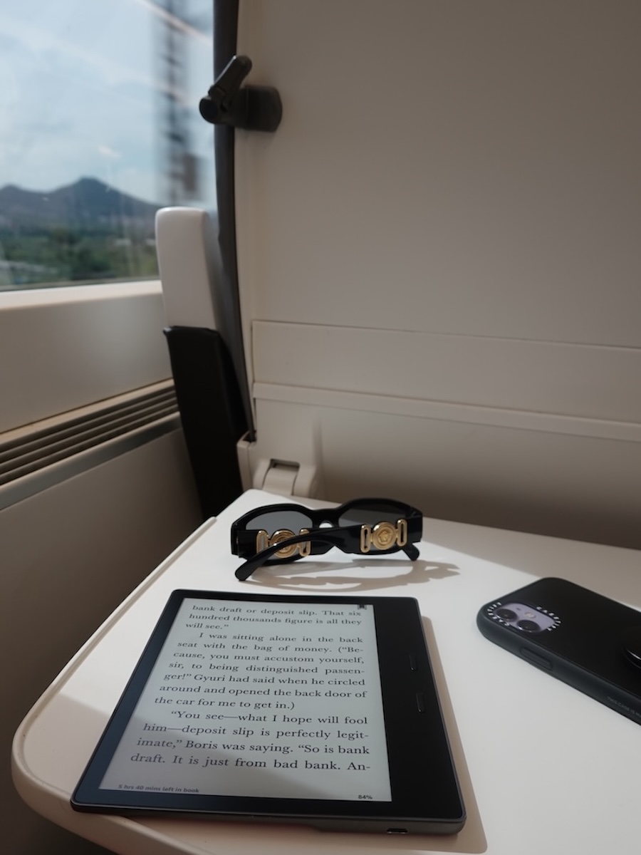 a kindle, glasses and a mobile on the seat table of the Euromed train which is How to get from Barcelona Airport to Valencia by train