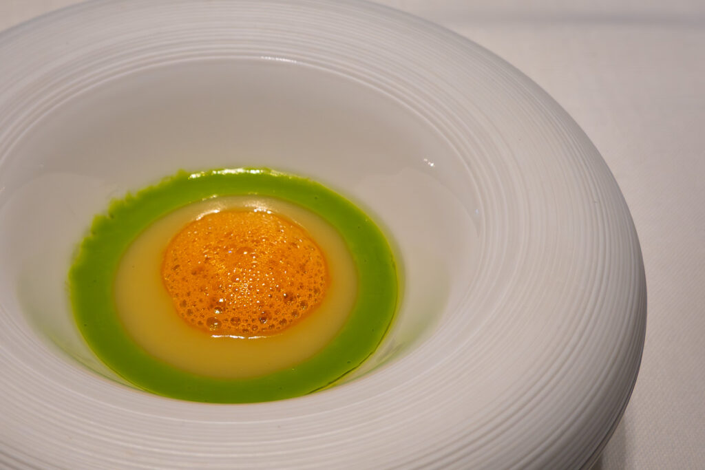 green, yellow and orange soup in a white plate from the fine dining Valencia experience at Ricard Camarena