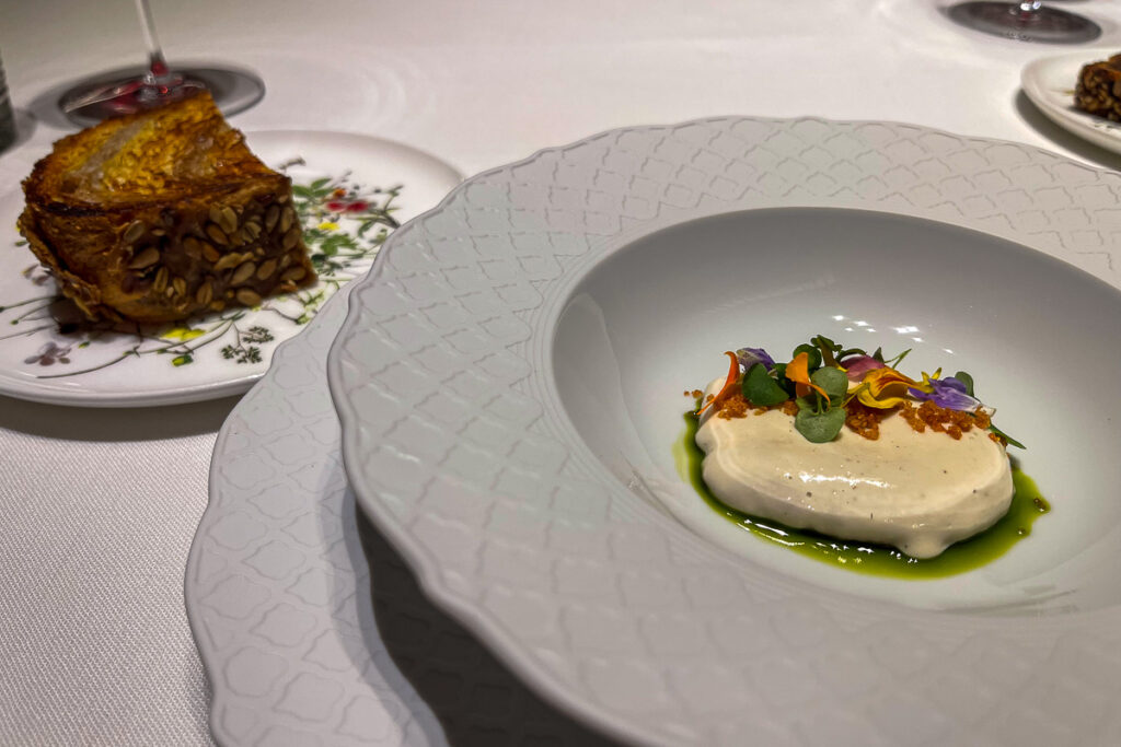 a plate with a melting cream and edible flowers with a bread on a side, this dish is one of the vegan fine dining Valencia Spain Ricard Camarena Oxalis 100% plant based menu