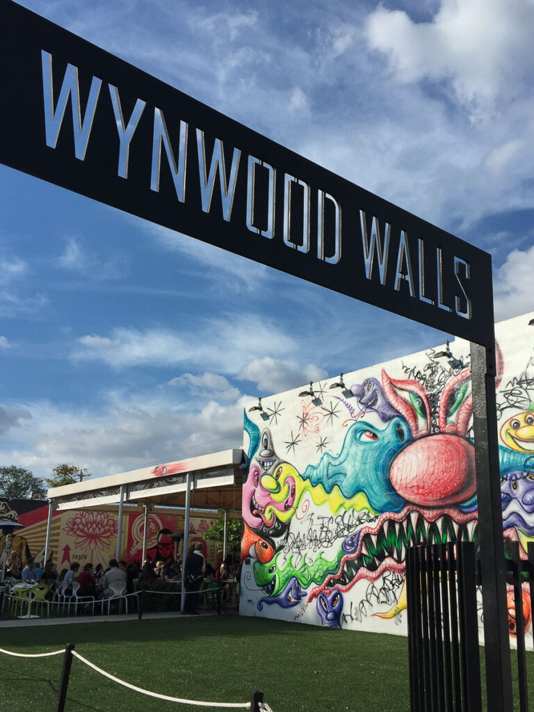 colorfull walls and a metal sign which is represent the wynwood walls miami which is a must spot to visit in a day in miami