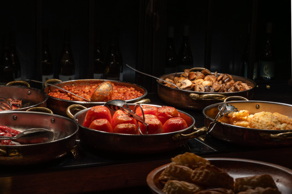 The warm breakfast station includes plant-based options like hash browns, mushrooms, and tomatoes which represents the Browns Central hotel Lisbon breakfast